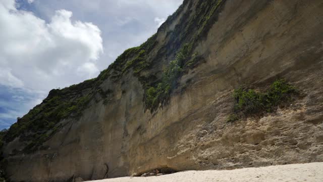 慢镜头盘左边的海洋冲浪和阳光明媚的海滩与轻轻碰撞的海浪和飙升的悬崖下的明亮的蓝色天空-努沙佩尼达&龙目岛，巴厘岛视频素材