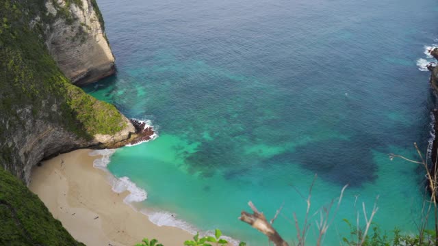 一个阳光明媚的热带海湾海滩，高耸的岩石悬崖，沙滩，绿松石的水域，和一个海洋延伸到地平线-努沙佩尼达和龙目岛，巴厘岛视频素材