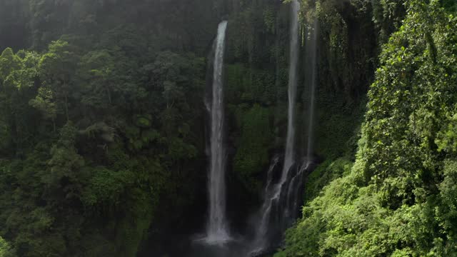 空中倾斜上升，环绕着茂盛的植物覆盖的悬崖和从山谷上升起的凉爽的薄雾的三瀑布-努沙佩尼达和龙目岛，巴厘岛视频素材