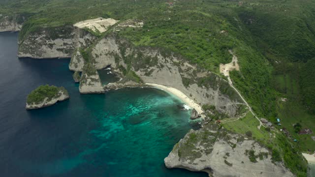 空中淘金沿着热带海滩海湾坐落在陡峭的悬崖边上，热带绿松石的水域，珊瑚，岩石，和阳光普照的树木-努沙佩尼达和龙目岛，巴厘岛视频素材