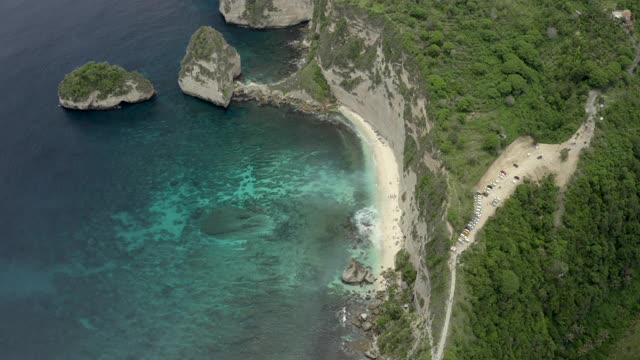 空中倾斜从热带海滩海湾坐落在陡峭的悬崖边上，热带绿松石的水域，珊瑚，岩石，和阳光普照的树木-努沙佩尼达和龙目岛，巴厘岛视频素材