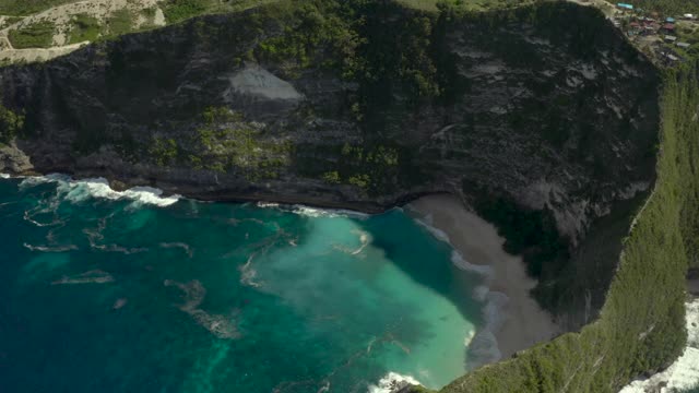 空中逆转戏剧性的热带海边悬崖景观，缓慢倾斜到海岸线，与拍打的海浪，突出的岩石和沙滩延伸到地平线-努沙佩尼达和龙目岛，巴厘岛视频素材