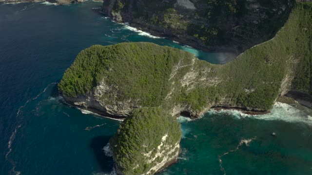 空中向前移动戏剧性的热带海岸悬崖景观与拍打的海浪，突出的岩石，诱人的绿松石水域，和沙滩-努沙佩尼达和龙目岛，巴厘岛视频素材