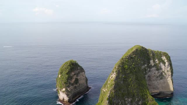 在一个阳光明媚的热带海湾海滩上，有高耸的岩石悬崖，沙滩，绿松石的水域，和延伸到地平线的海洋-努沙佩尼达和龙目岛，巴厘岛视频素材