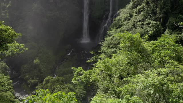 空中向前移动，盘旋而上的是一个被郁郁葱葱的植物覆盖的悬崖和从下面山谷升起的凉爽的薄雾所包围的三个瀑布——努沙佩尼达和龙目岛，巴厘岛视频素材