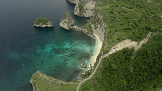 空中倾斜到热带海滩海湾坐落在陡峭的悬崖边上，热带绿松石的水域，珊瑚，岩石，和阳光普照的树木-努沙佩尼达和龙目岛，巴厘岛视频素材