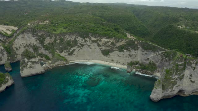 空中淘金穿过热带海岸线，海滩嵌套在高耸的悬崖上，绿松石般的水域，起伏的山丘直到地平线-努沙佩尼达和龙目岛，巴厘岛视频素材