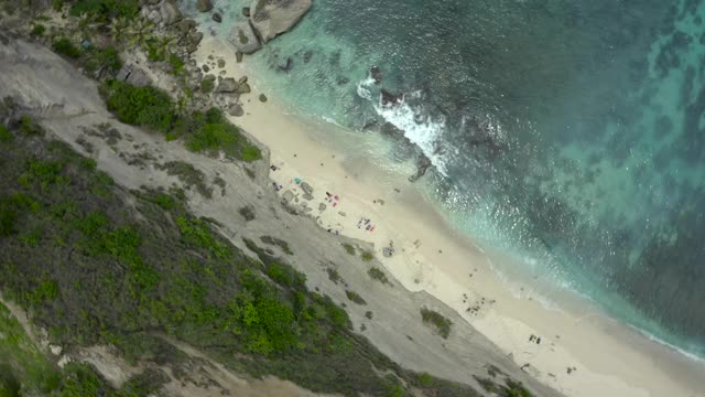 空中旋转沿着海滩悬崖边的崩溃的屋檐，绿松石的水，和日光浴在阳光浸泡的圣努沙佩尼达和龙目岛，巴厘岛视频素材