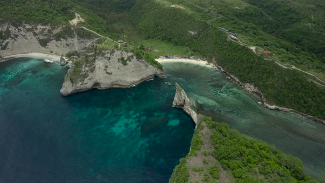 空中淘金沿着热带海滩海湾左边坐落在陡峭的悬崖边上，热带绿松石的水域，珊瑚，岩石和阳光普照的树木-努沙佩尼达和龙目岛，巴厘岛视频素材