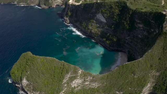 空中淘金高过陡峭的悬崖和热带海湾的拍打的海浪，突出的岩石，诱人的绿松石水域，和沙滩-努沙佩尼达和龙目岛，巴厘岛视频素材