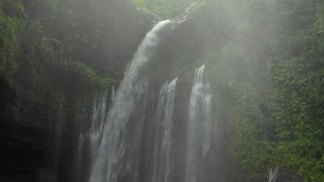 在巴厘岛努沙佩尼达和龙目岛，空中翱翔的瀑布被茂密的热带树叶和上升的薄雾和岩架包围着视频素材