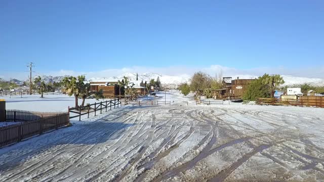 空中拍摄的城镇覆盖着雪对蓝色的天空，无人机在阳光明媚的一天在公路上飞行-乔舒亚树，加利福尼亚视频素材