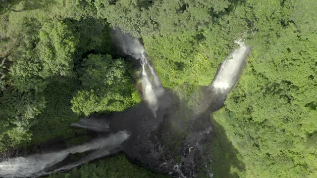 空中旋转远离翱翔的三重瀑布，跌落盆地的梯田和热带雨林的树冠-努沙佩尼达&龙目岛，巴厘岛视频素材