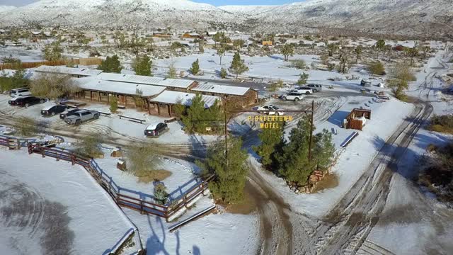 空中摇摄汽车旅馆招牌上的轮胎印在镇上的雪地上，无人机在阳光明媚的一天飞近建筑物对抗雪山-约书亚树，加利福尼亚视频素材