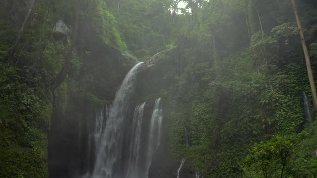 从飞流直下的瀑布空中倒转，沿着陡峭的山谷墙壁、岩石、茂密的树叶和上升的薄雾奔流而行——努沙佩尼达和龙目岛，巴厘岛视频素材