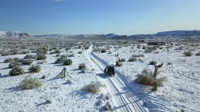 航拍的车辆在积雪覆盖的道路到达城镇，无人机飞向雪山对蓝天-约书亚树，加利福尼亚州视频素材