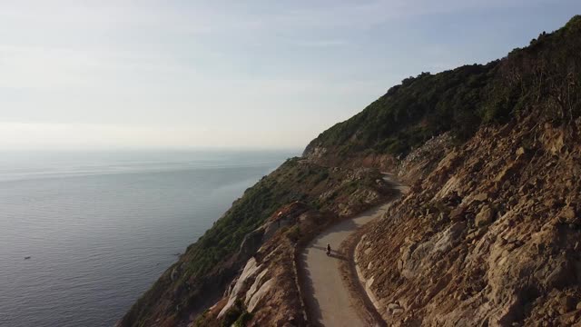 鸟瞰图的摩托车驾驶沿海岸道路上的一个岛屿的悬崖边。视频素材