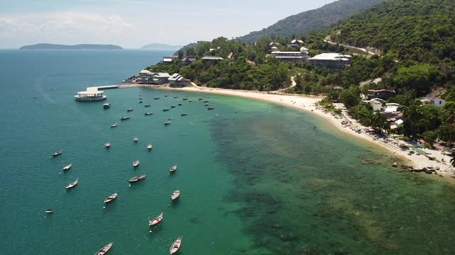 无人机俯瞰一个热带岛屿的海岸海滩，水面上漂浮着船只。视频素材