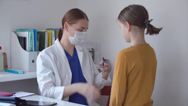 女医生戴着医用口罩，用听诊器听小女孩的肺音视频素材