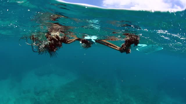 水下近距离拍摄的碎片与海洋生物纠缠在一起，漂浮在海面上，轻轻摇曳的海水和一个明亮的阳光灿烂的天空——夏威夷瓦胡岛视频素材