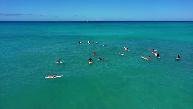 空中封锁拍摄人们在碧蓝的天空下在碧绿的海面上冲浪，无人机在阳光灿烂的日子里飞过冲浪者——夏威夷的瓦胡岛视频素材