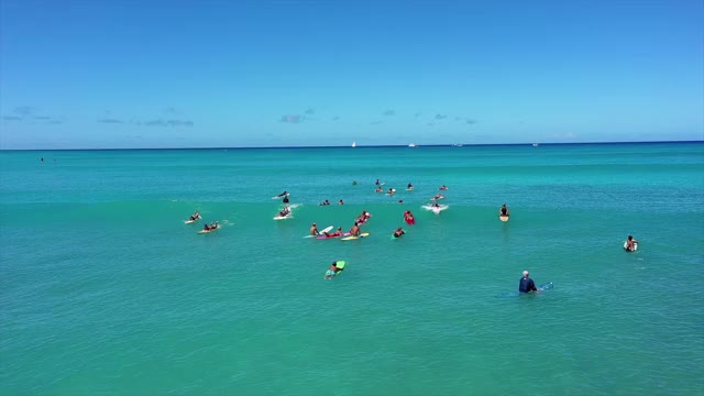 空中平移拍摄冲浪者享受晴朗的一天在海上对天空，无人机飞过人们冲浪海浪-瓦胡岛，夏威夷视频素材