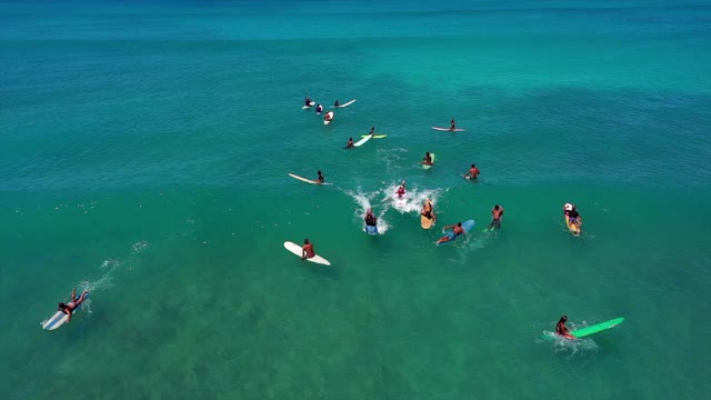 在阳光明媚的日子里，人们在海浪上冲浪时的空中镜头，无人机飞过碧绿的海面上的冲浪者——夏威夷瓦胡岛视频素材