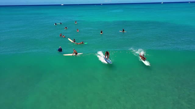 空中平移拍摄的人冲浪海浪对蓝色的天空，无人机向后飞行冲浪者在绿松石海在阳光明媚的一天-瓦胡岛，夏威夷视频素材