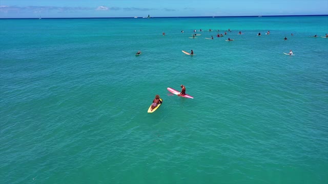 空中倾斜向下拍摄的冲浪者在绿松石海在阳光明媚的一天，无人机向前飞向人们冲浪对天空-瓦胡岛，夏威夷视频素材