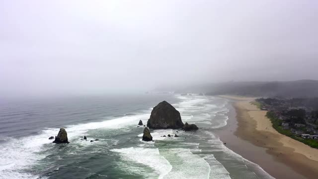 空中平移拍摄的海浪溅在海滩上对多云的天空，无人机飞过海岸附近的城市-坎农海滩，俄勒冈州视频素材