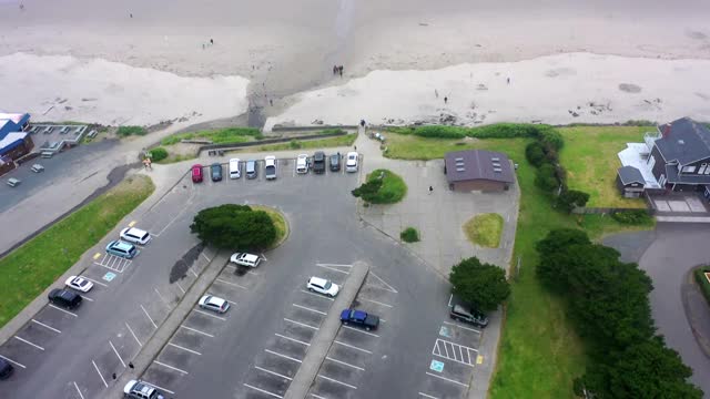 空中倾斜拍摄的停车场和房屋在城市的海滩，无人机飞向海浪溅在天空，俄勒冈州坎农海滩视频素材