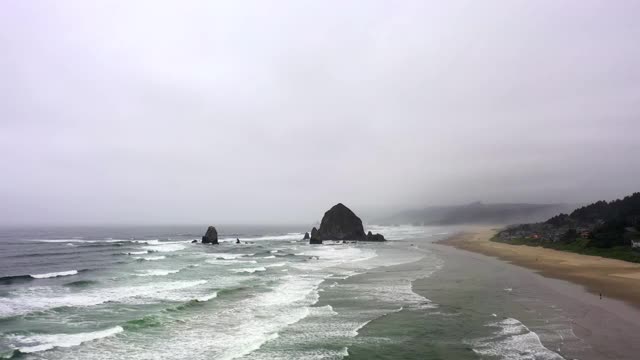 航拍海浪溅在海滩上对多云的天空，无人机在海岸附近的城市-坎农海滩，俄勒冈州向前飞行视频素材