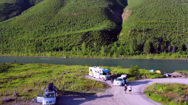 空中拍摄的人和车辆在河岸上的营地，无人机上升附近的河流对绿色的山在阳光明媚的一天-大北方平原，MT视频素材