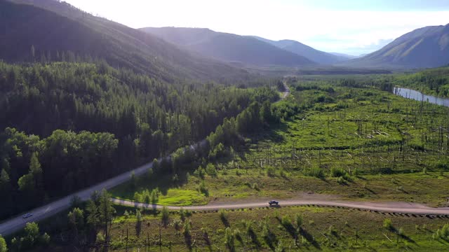 空中拍摄的车辆在绿树林中的道路上，无人机在阳光明媚的一天飞向山脉-大北方平原，MT视频素材