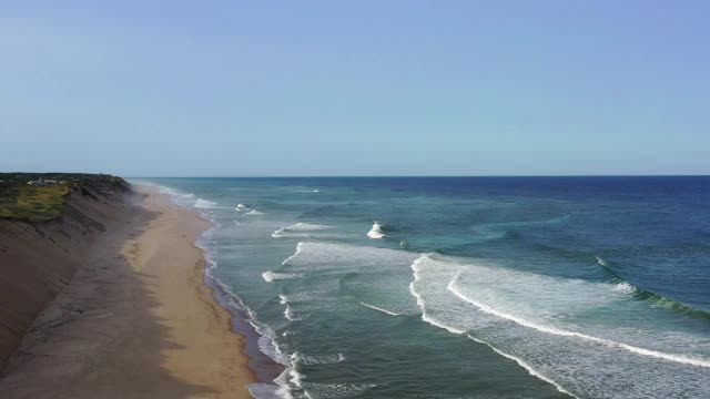 航拍的人在海滩上的海岸城镇对着蓝天，无人机飞在海浪溅在岸边-科德角，马萨诸塞州视频素材