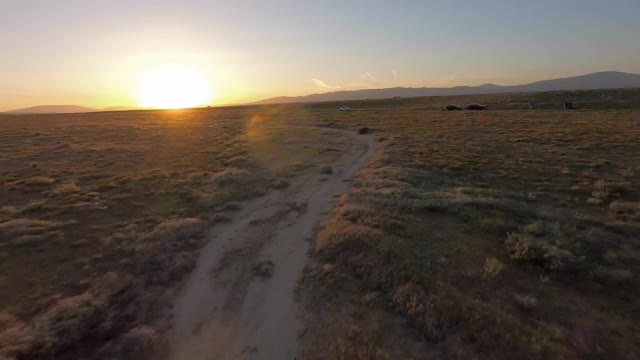 空中低空快速移动，沿着一条土路，穿过一个宽阔的干燥山谷平原，在黄昏的时候，有灌木丛，野花，和起伏的山丘——羚羊谷，加利福尼亚视频素材