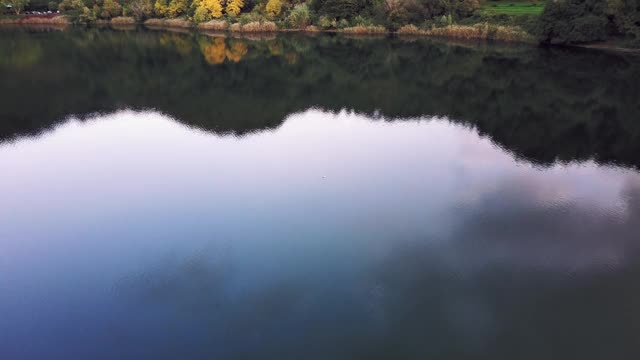 空中平移拍摄的树木在湖岸附近的山脉，无人机向前飞行的湖对天空视频素材