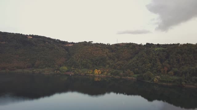 空中平移拍摄的树木在湖岸附近的山脉，无人机向前飞行的湖对天空视频素材