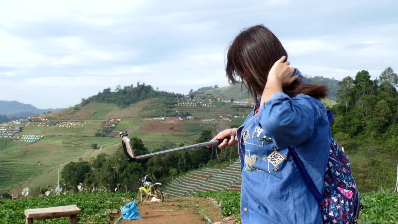 年轻的亚洲女性游客用自拍杆上的智能手机自拍视频素材