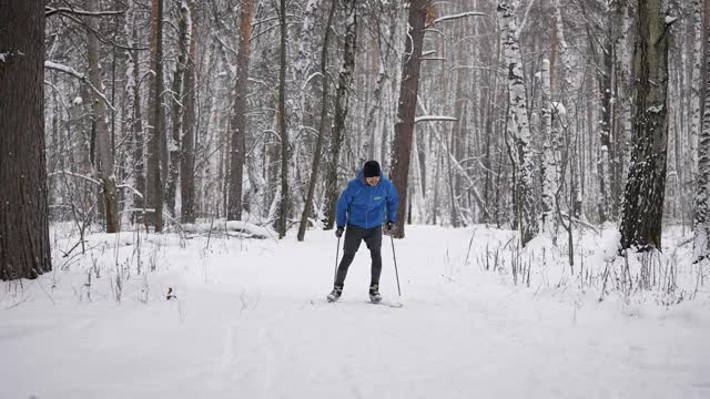 一个年轻人正在冬季森林里进行越野滑雪。运动员滑冰。视频素材