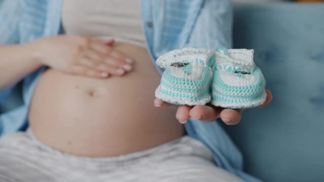 慢动作特写的女人的手拿着小婴儿靴子和抚摸怀孕的肚子视频素材