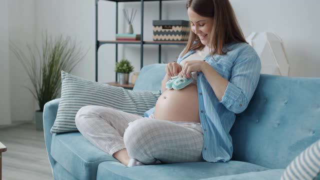 可爱的孕妇玩婴儿靴子在肚子上走在家里玩视频素材