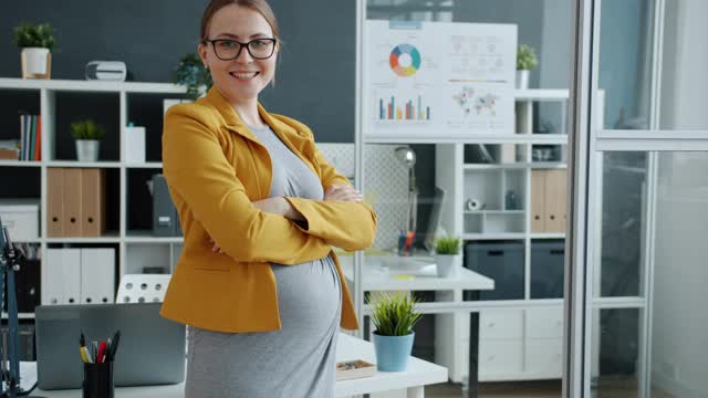 年轻的怀孕女商人站在办公室双臂交叉微笑的肖像视频素材