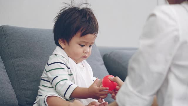 亚洲父母和男婴在家里的客厅玩塑料球视频下载