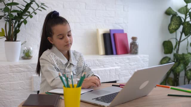 特写照片的小漂亮小学生学校聊天skype笔记本网上课视频电话坐在书桌，距离，同学隔离学习客厅室内视频素材