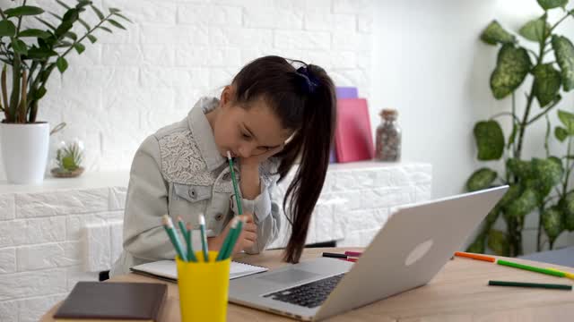 特写照片的小漂亮小学生学校聊天skype笔记本网上课视频电话坐在书桌，距离，同学隔离学习客厅室内视频素材