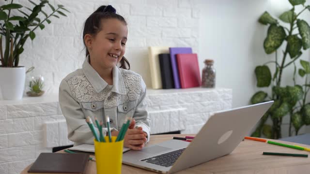 特写照片的小漂亮小学生学校聊天skype笔记本网上课视频电话坐在书桌，距离，同学隔离学习客厅室内视频素材