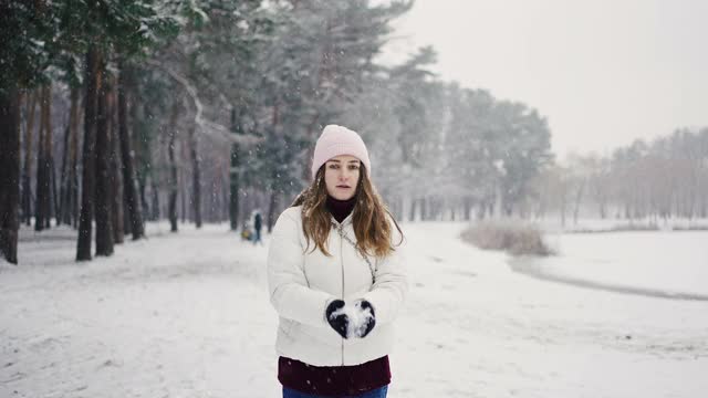 年轻女子把雪抛起来，在雪下打转，在森林里玩，慢镜头视频素材