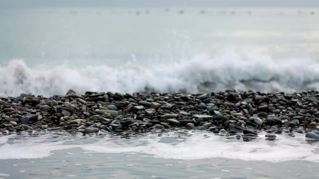 海浪拍打在卵石滩上。镜头的焦点从海岸转移到地平线，那里有一群鸟在游泳。缓慢的运动。冬季视频素材