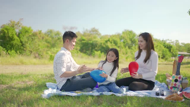 幸福的家庭亚洲父亲，母亲和小女孩玩气球，并享受了我们一起在野餐布在绿色的花园。一家人在大自然中享受阳光明媚的秋日。视频素材